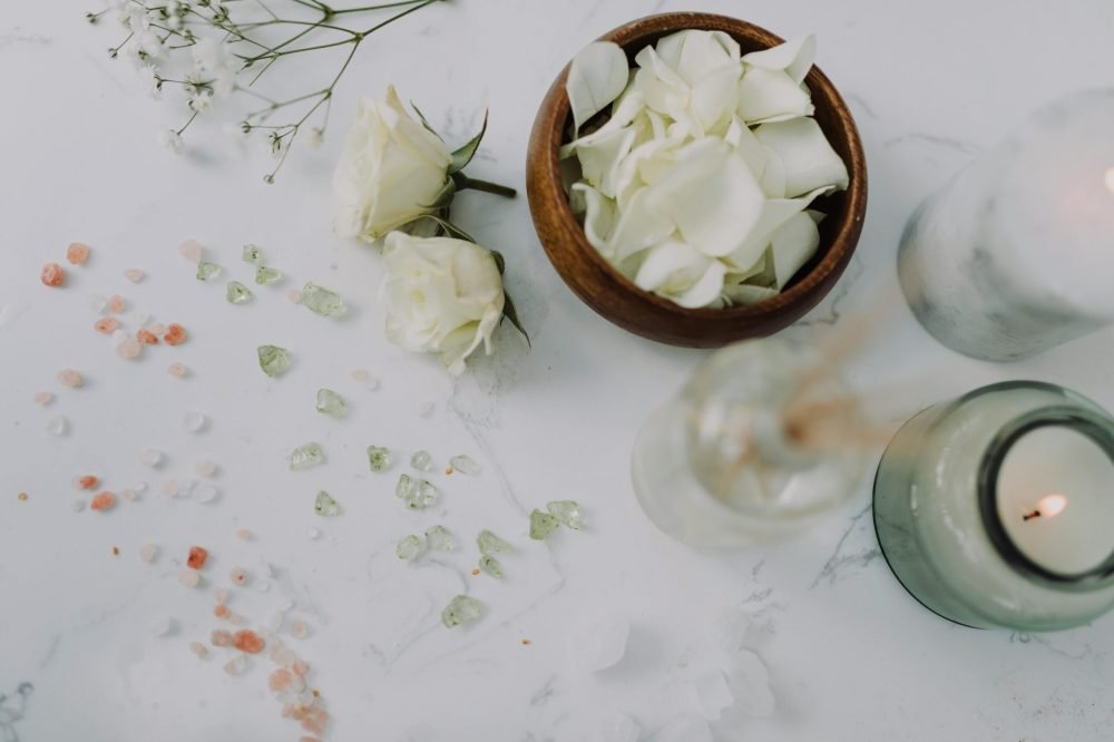 Aesthetic flat lay of white roses, petals, candles, and decorative accents on marble.